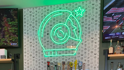 Bar setting with a neon sign, beer taps, and a coffee cup on a counter.