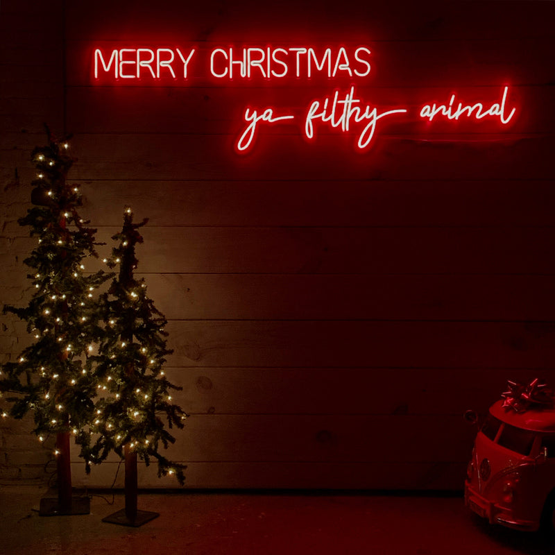 Neon sign with 'Merry Christmas ya filthy animal' text next to a decorated Christmas tree and gift box.