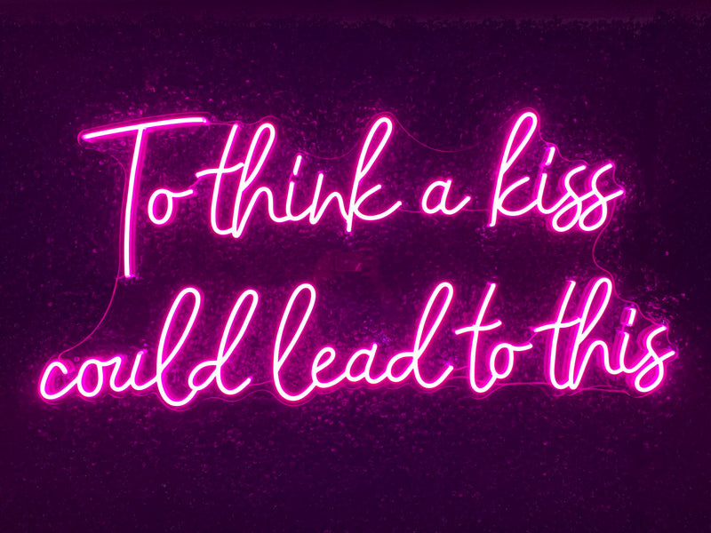 Neon sign with the text 'To think a kiss could lead to this' on a dark background