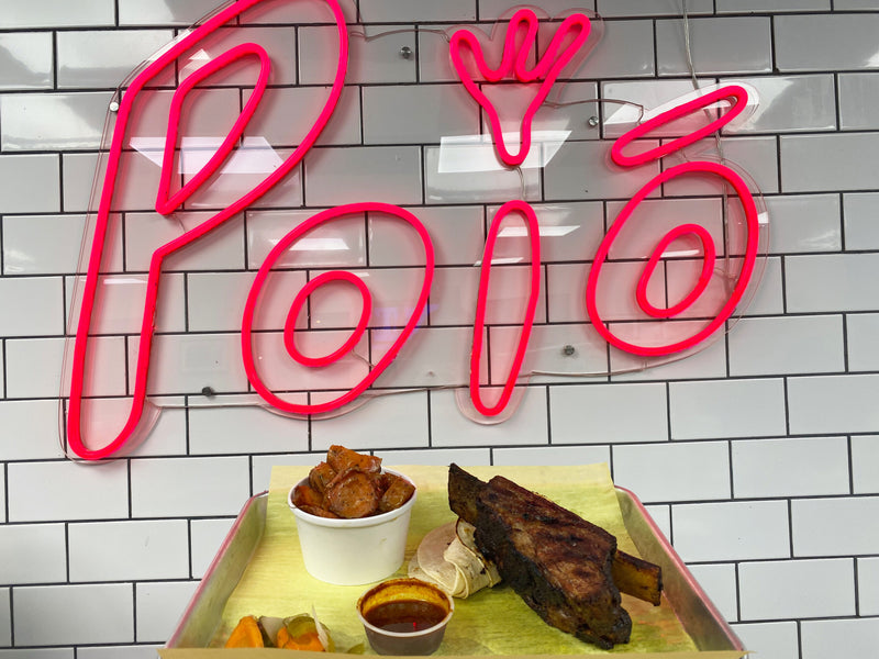 Neon sign with 'Poio' on a tiled wall above a tray of food.