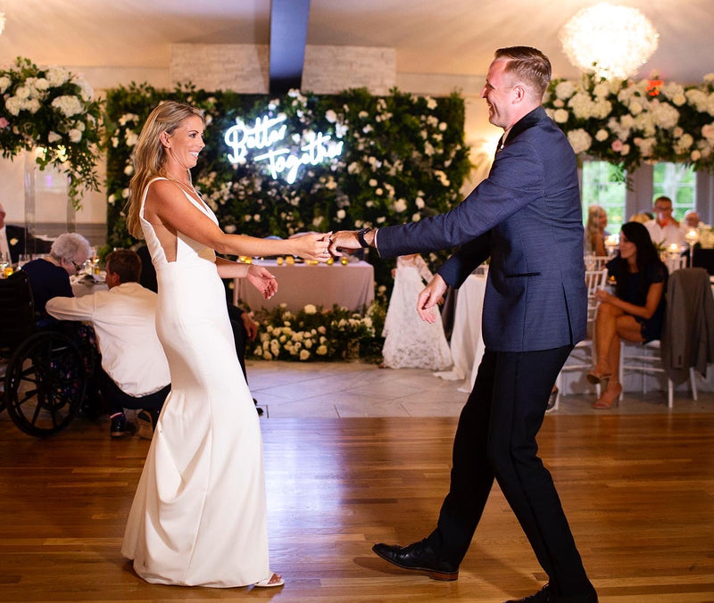 Man and woman dancing in a decorated indoor setting with floral arrangements and people in the background.
