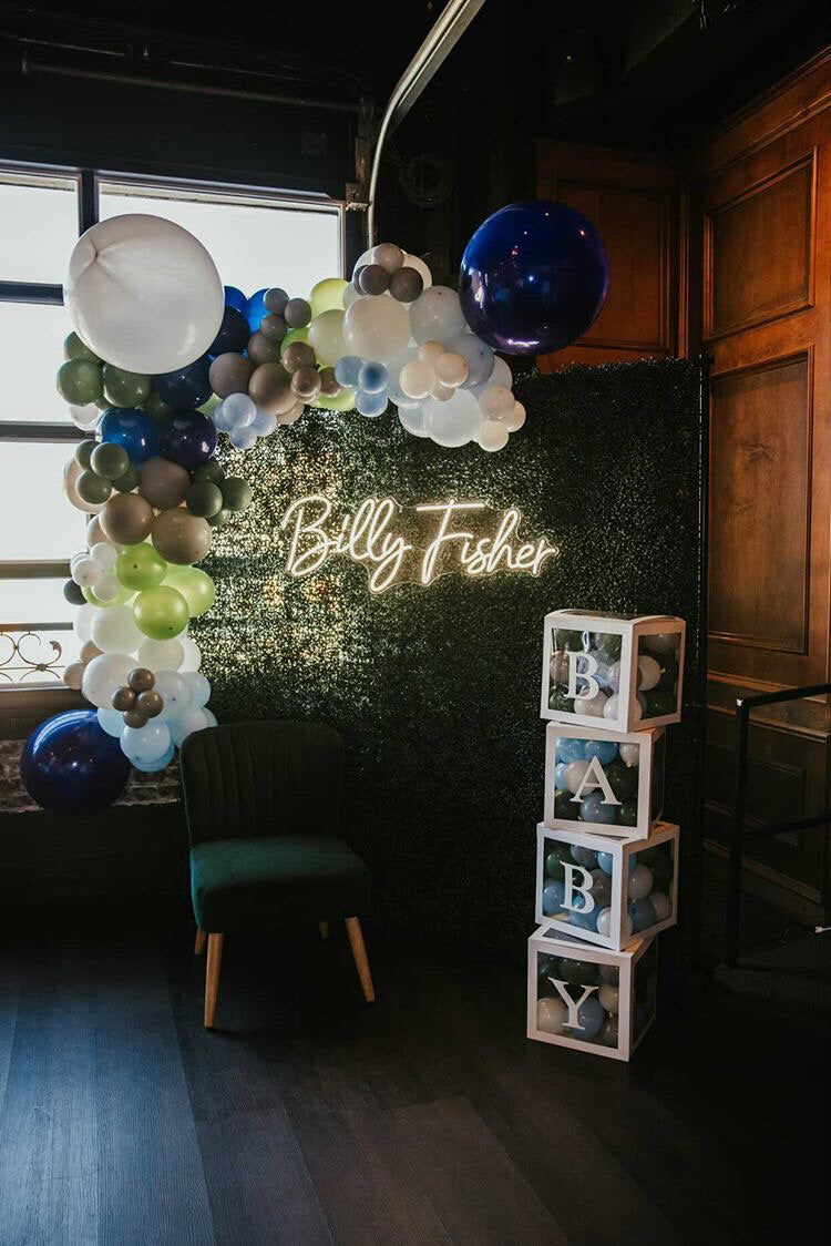 Decorative setup with balloons, a neon sign, and baby blocks in a room.