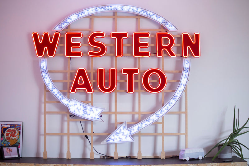 Neon sign with 'Western Auto' text and arrow design on a white wall.