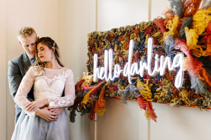 Couple standing in front of a colorful wall with 'hello darling' sign